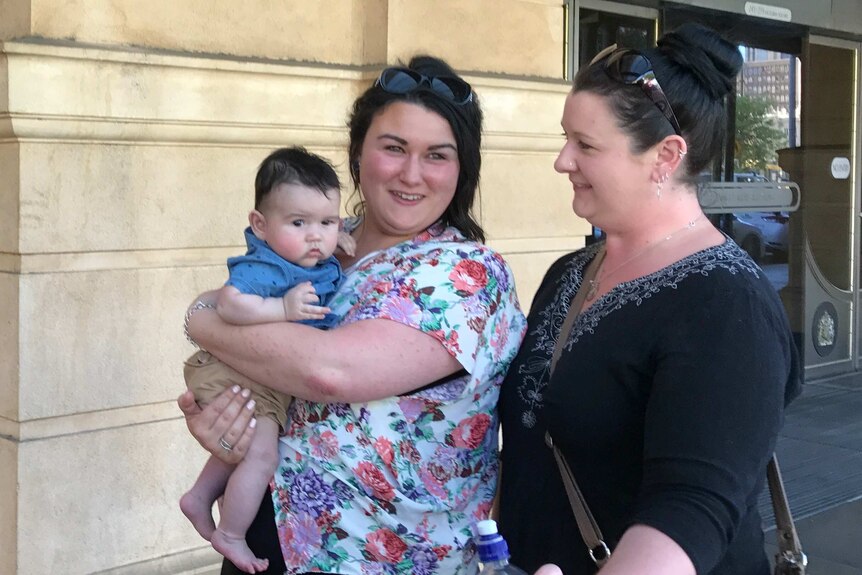 Two women, one holding a baby, leave the Adelaide courts