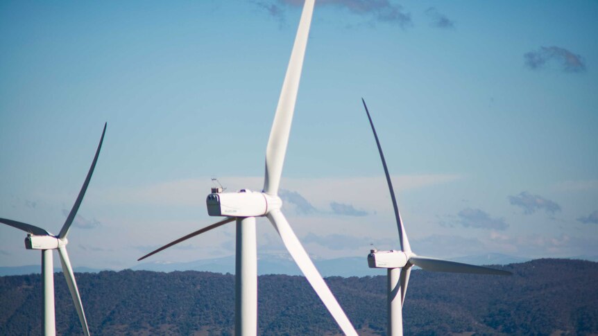 Three large wind turbines against a country mountain backdrop.