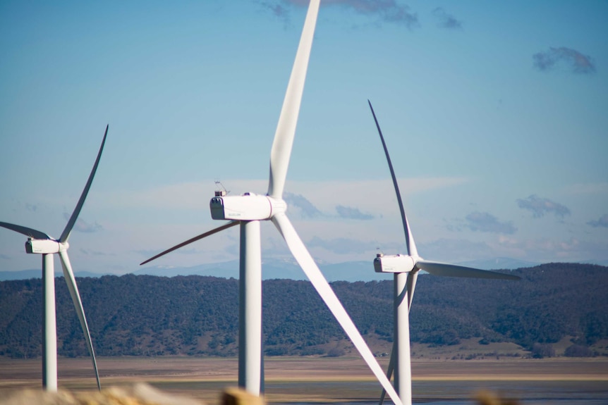 Three large wind turbines against a country mountain backdrop.