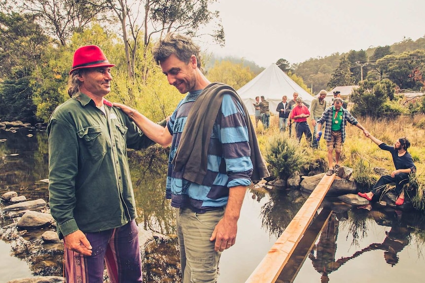 Men help each other across a creek Crossing the creek - Men with Heart exhibition.