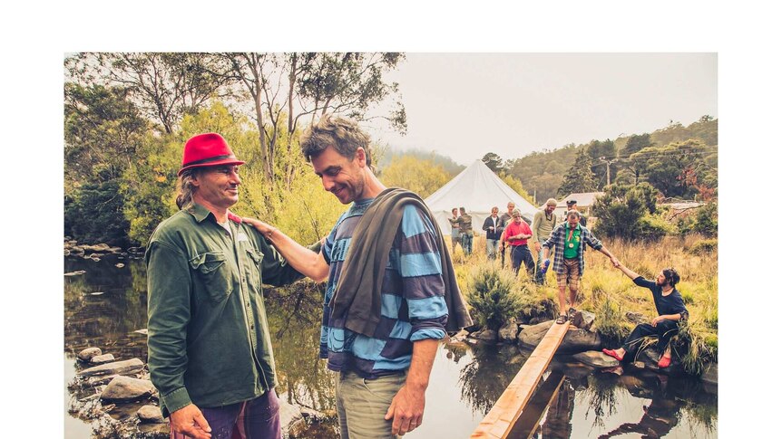 Men help each other across a creek Crossing the creek - Men with Heart exhibition.