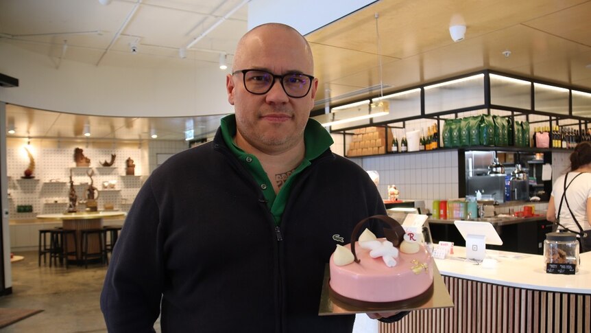 Cafe owner Pierrick Boyer holding up a pink cake in his cafe.
