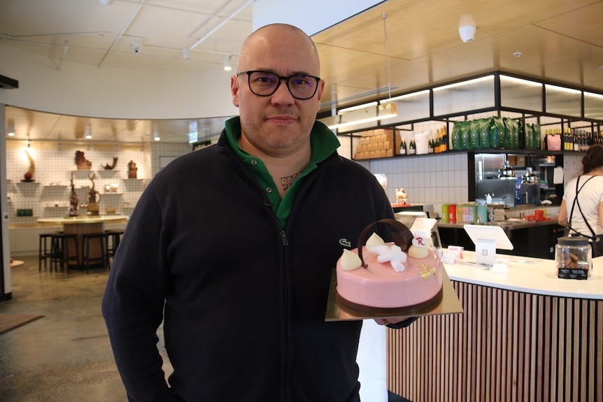 Cafe owner Pierrick Boyer holding up a pink cake in his cafe.