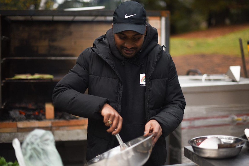 John Chinsami cooks chicken skewers and sausages on a barbecue