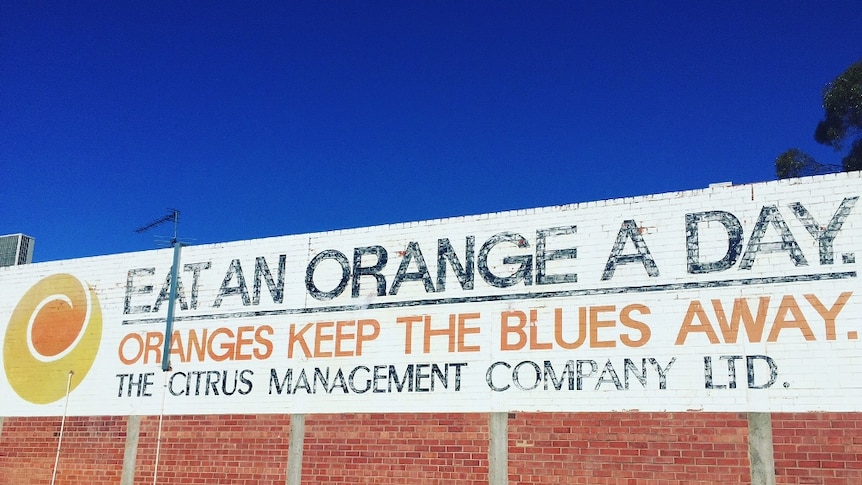 Large sign on the side of building reads 'Eat an orange a day. Oranges keep the blues away. The Citrus Management Company Ltd."