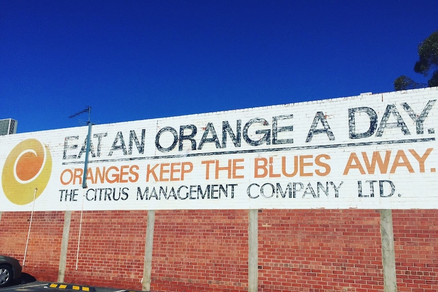 Large sign on the side of building reads 'Eat an orange a day. Oranges keep the blues away. The Citrus Management Company Ltd."
