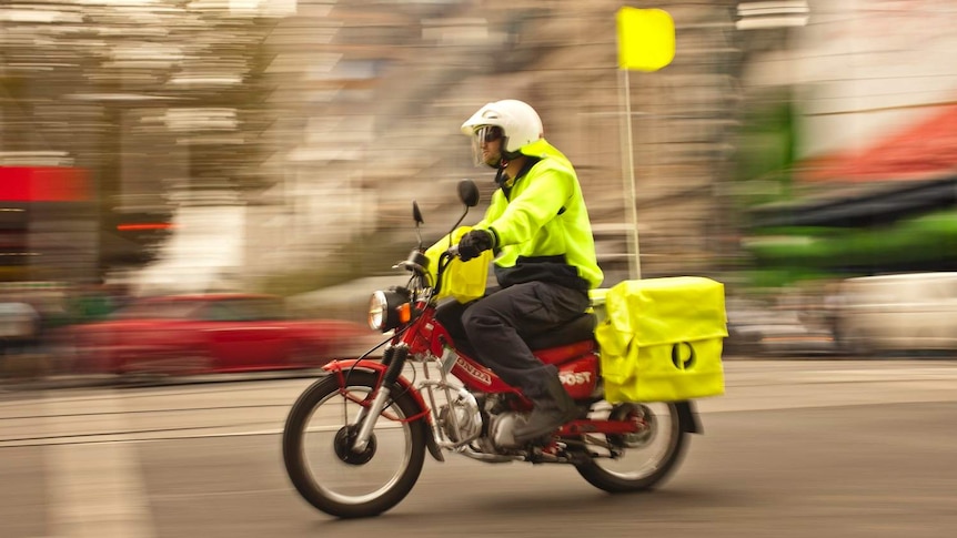Postman wears yellow high vis, with the background blurred to show speed.