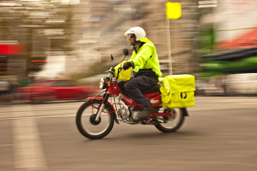 Postman wears yellow high vis, with the background blurred to show speed.