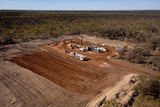 An aerial view of several lines of trucks parked on a large, cleared patch of dirt, surrounded by scrub.