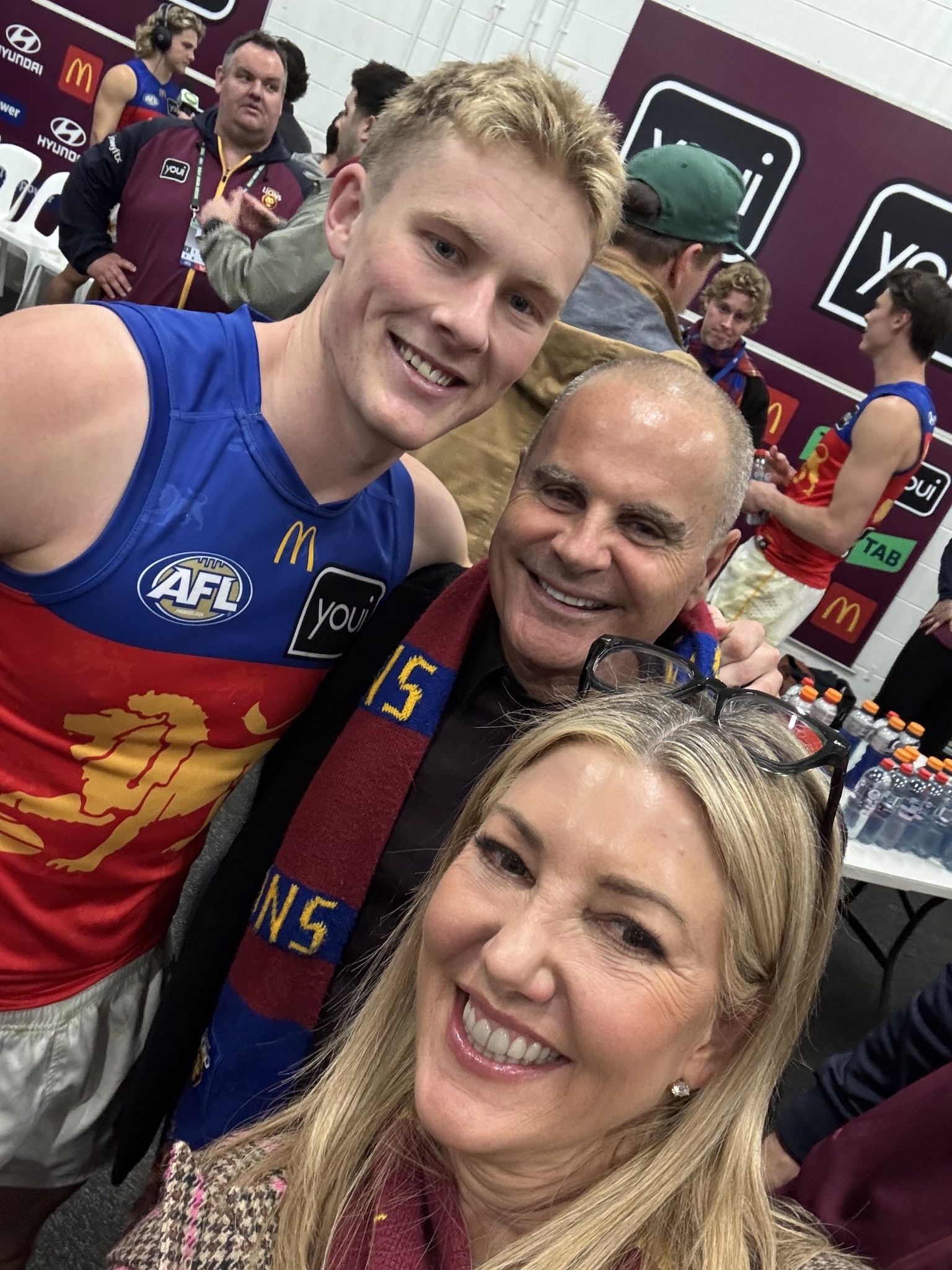 A woman and a man take a selphie with a football player in a blue and red jersey with a yellow lion on it.