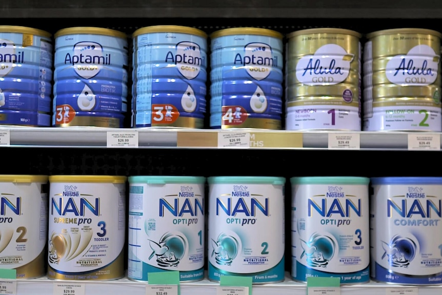 Tins of infant and toddler formulae sitting on shelves in a pharmacy.