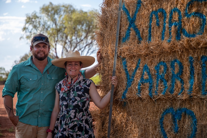 a man stands next to a woman next to square bales painted with the word XMAS