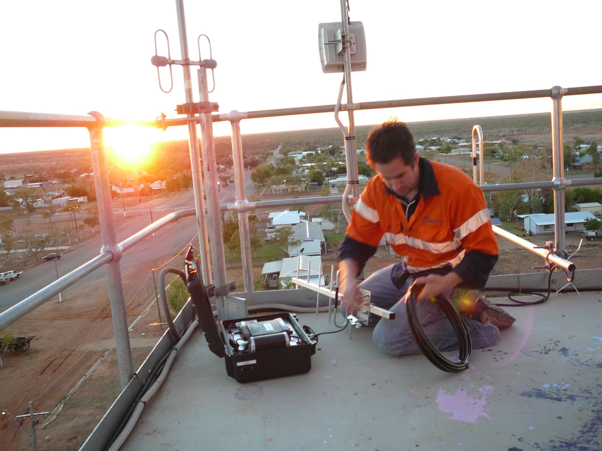 Um homem em alta visibilidade opera uma antena enquanto trabalha no telhado de uma cidade rural.