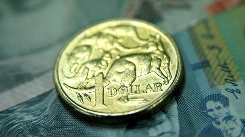 Australian one dollar coin sits on an Australian 20 dollar and 50 dollar note