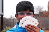 Young boy with glasses holding a flush of cards up to his face