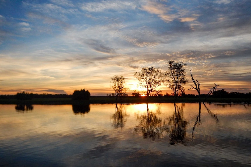 The sun setting over the Kakadu wetlands with clouds in the sky.