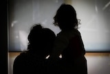 The silhouette of a woman leaning and holding a child.