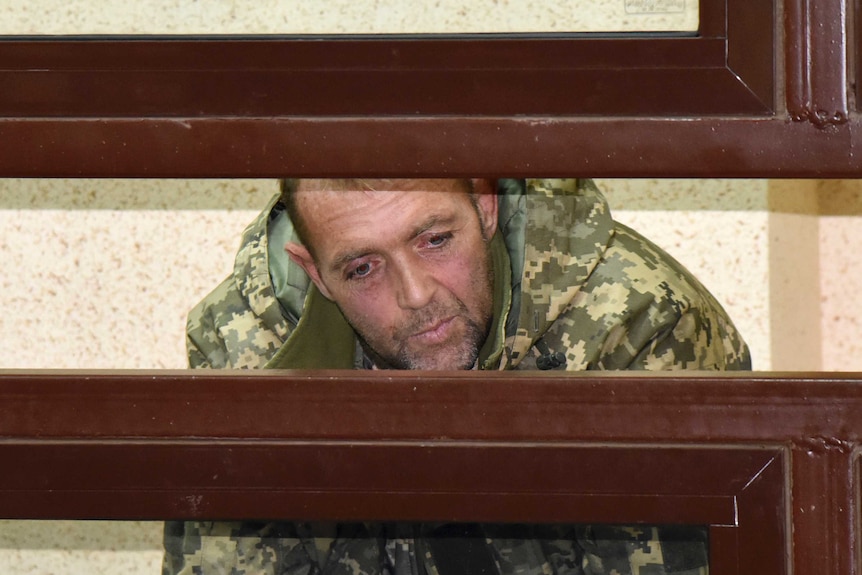 A captured Ukrainian sailor sits behind bars in a court room.