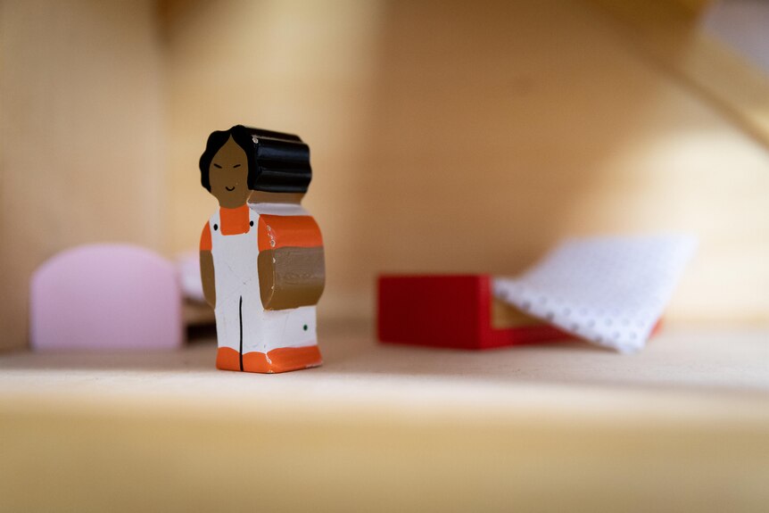 A figurine of a young girl in a messy bedroom in a miniature wooden house.