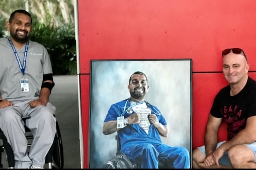 Man squatting beside painting of a man in a wheelchair.