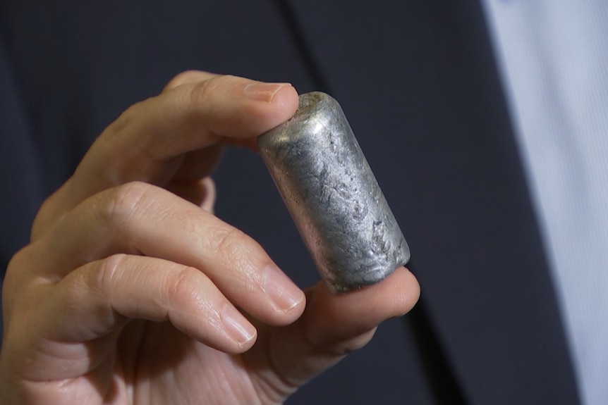 A hand holds a small capsule-shaped piece of metal.