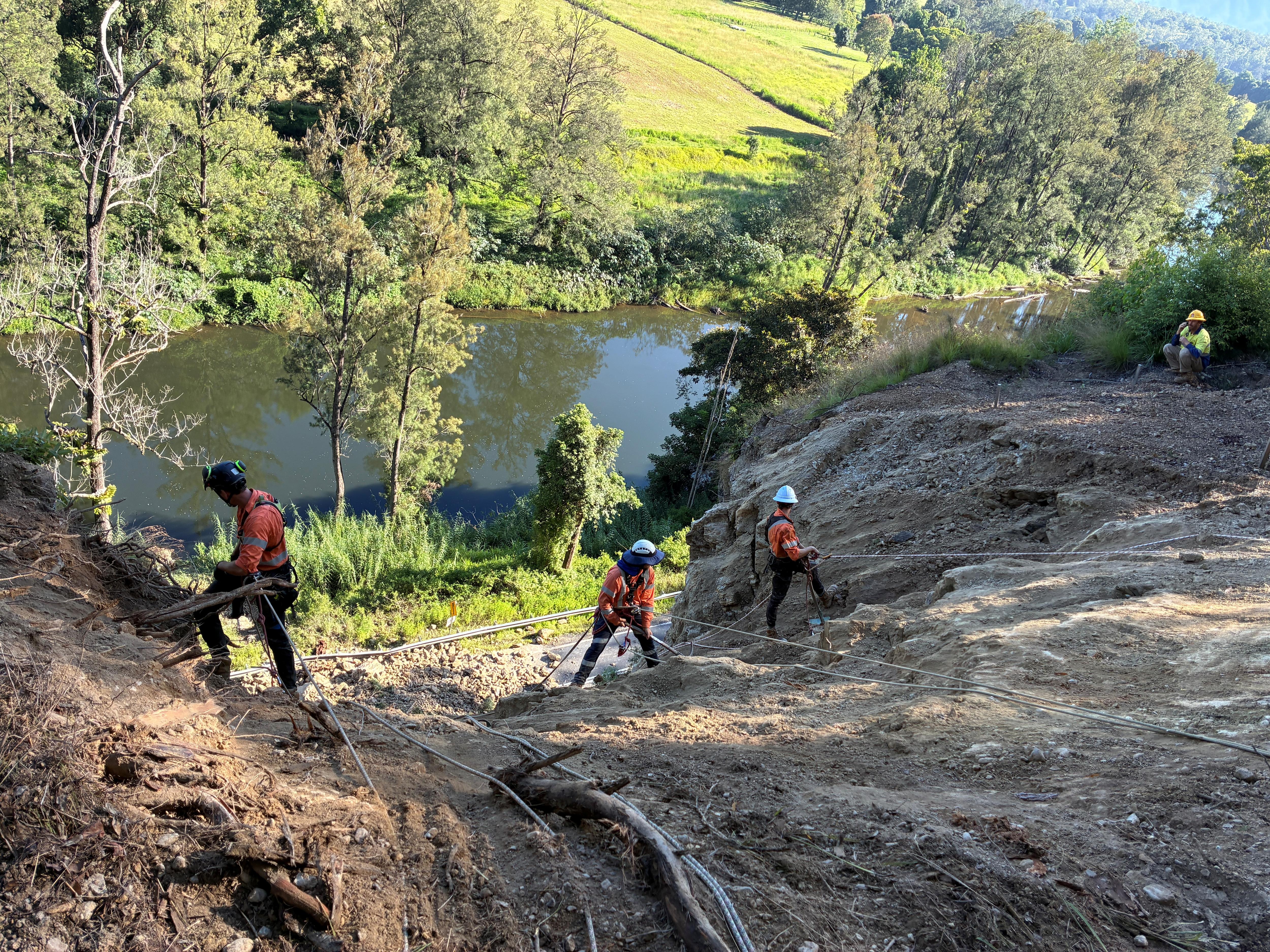 Tres personas con camisas de trabajo de color naranja cuelgan de cuerdas en un deslizamiento de tierra.