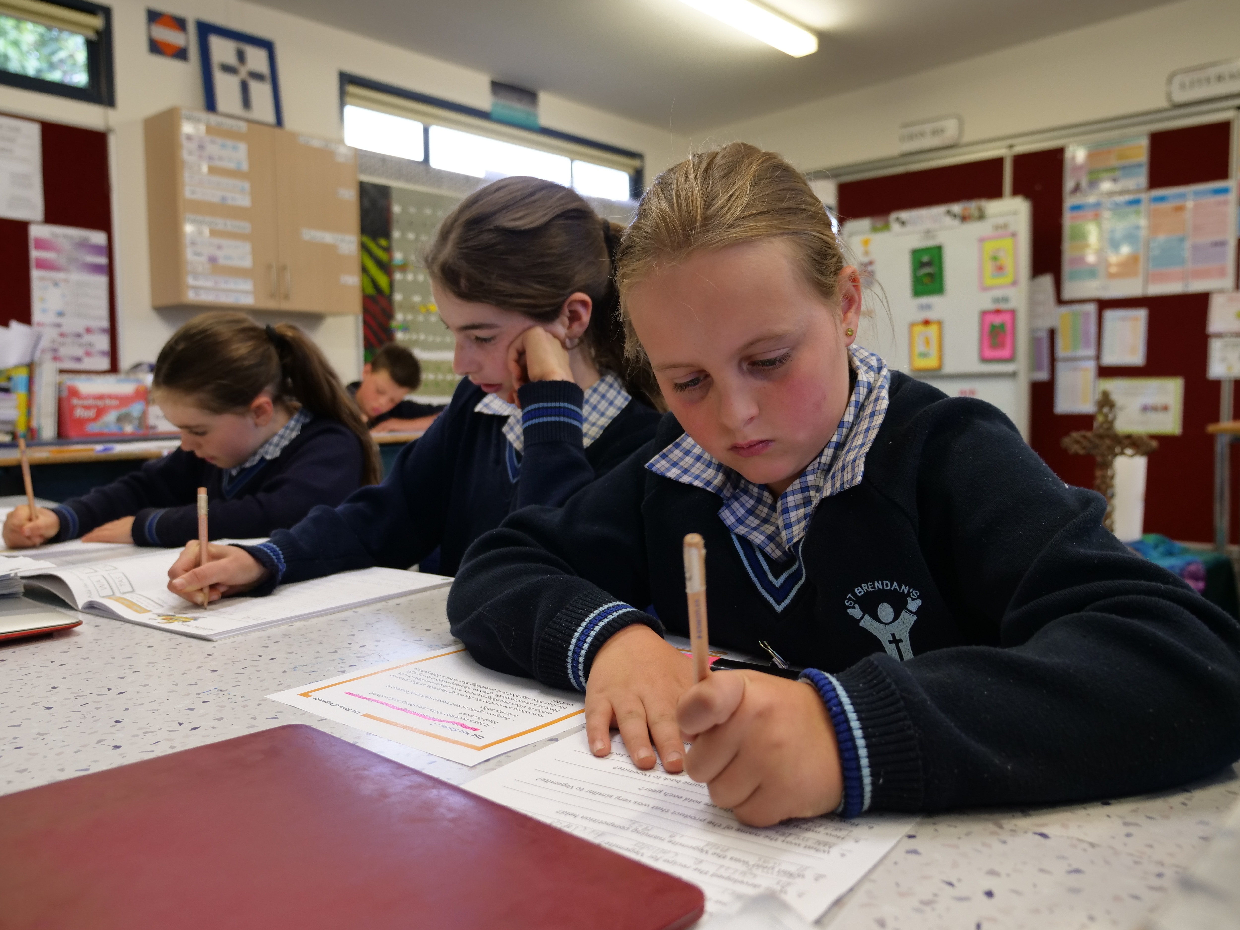 A girl in school uniform sits at a desk and writes