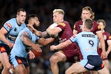 A man in Maroon with a ball in his arm breaks through opponent tackles