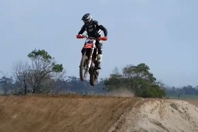 A dirt bike rider flies off a mound.