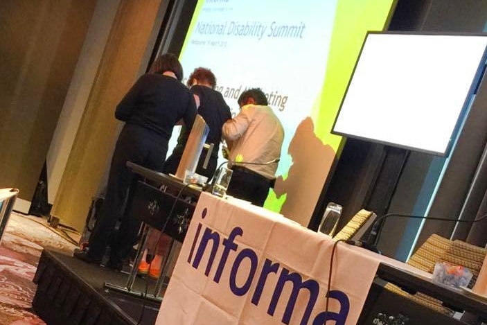 A speaker is helped by two people off the stage at the National Disability Summit.