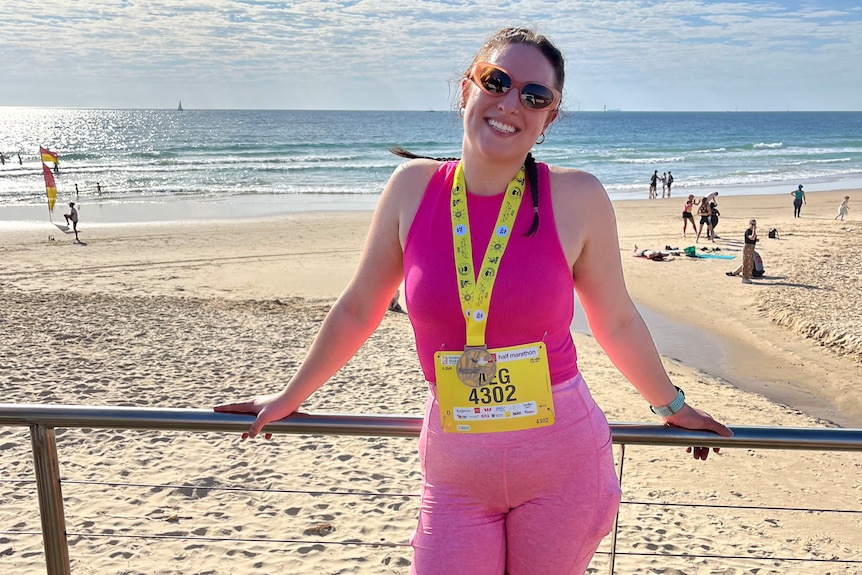 A woman wearing pink singlet and shorts and a medal around her neck at the beach.