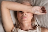 A woman holds her arm to her forehead while laying on a bed.
