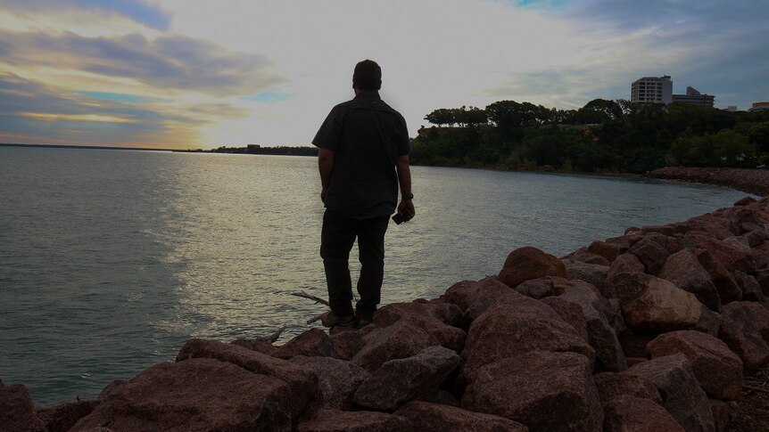 A man stands by Darwin Harbour staring into the water.