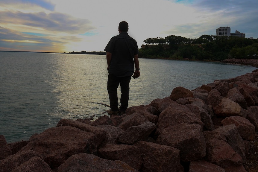 A man stands by Darwin Harbour staring into the water.