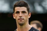 A Collingwood AFL player walks while teamates and opposition players are behind him.