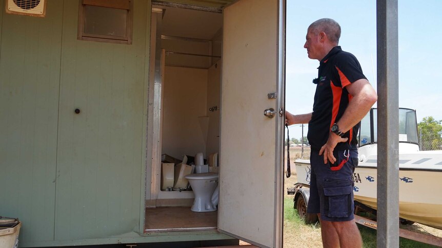 Ian Chamberlain is standing in front of a open toilet door. Inside, there is plumbing parts everywhere.