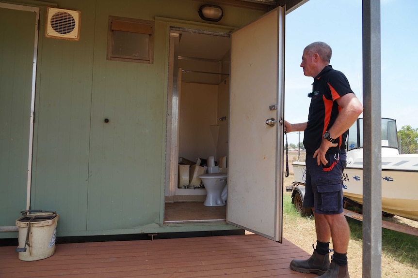 Ian Chamberlain is standing in front of a open toilet door. Inside, there is plumbing parts everywhere.