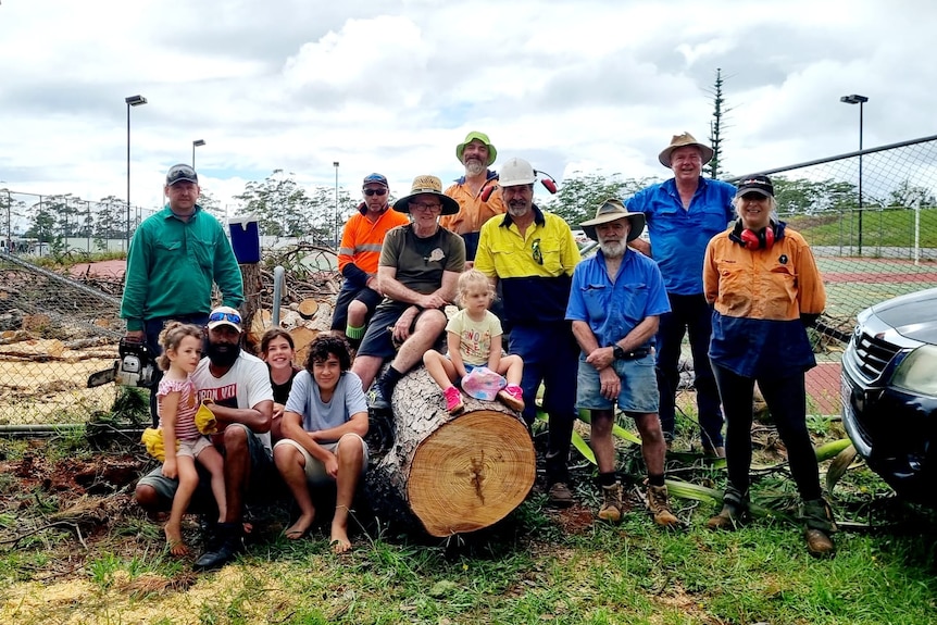 A group of people sitting on a large tree that has been cut up by chainsaws. 