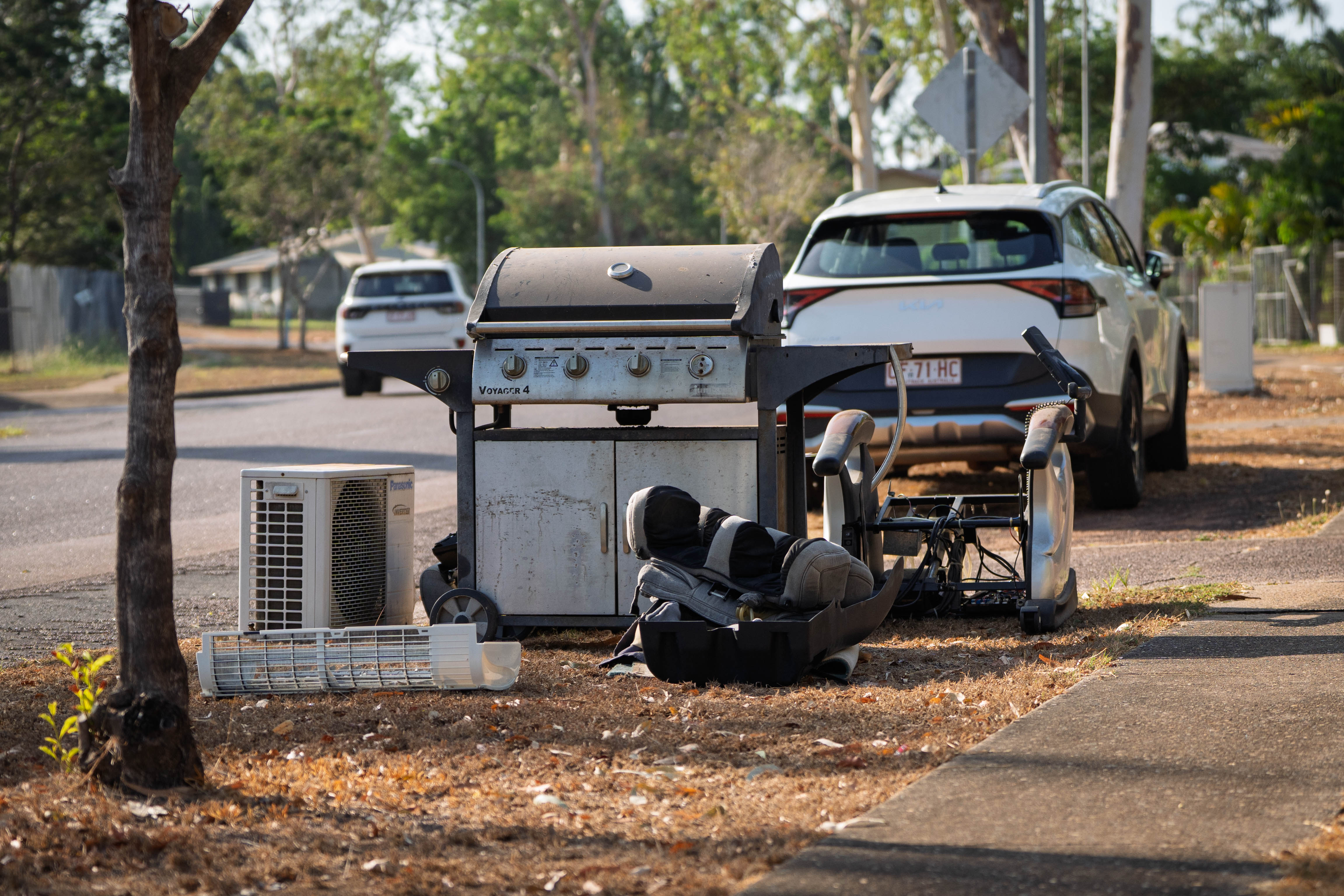 A number of discarded items, including an old barbecue and air-conditioning unit, sit kerbside awaiting collection.