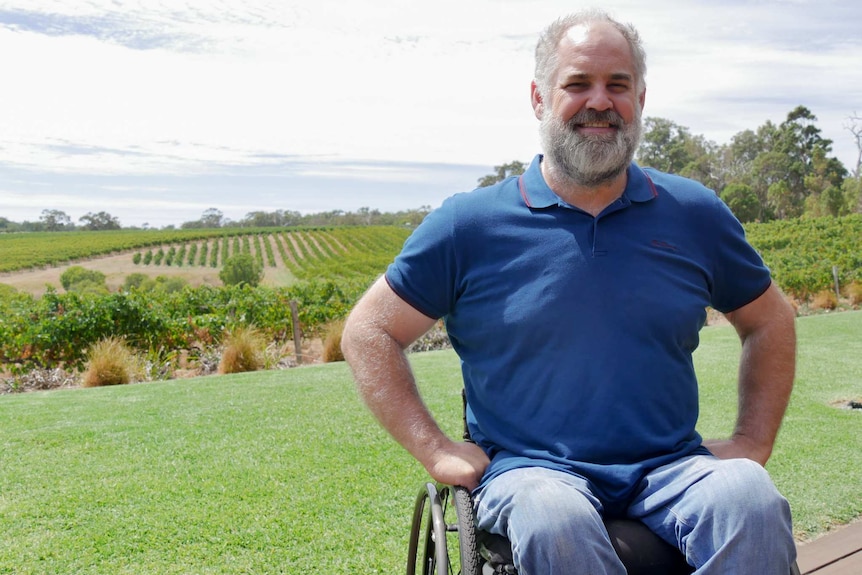 A man in a wheelchair with grape vines in the background.