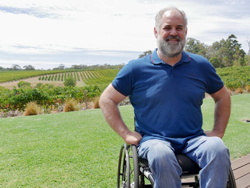 A man in a wheelchair with grape vines in the background.