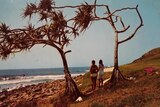 Two girls standing on a coastal headland watching surfers and waves on the point.