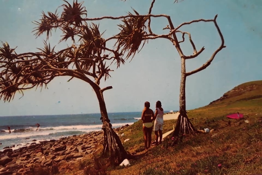 Two girls standing on a coastal headland watching surfers and waves on the point.