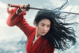 A woman with wind-swept hair looks fiercely off-camera, holding a sword about her head.