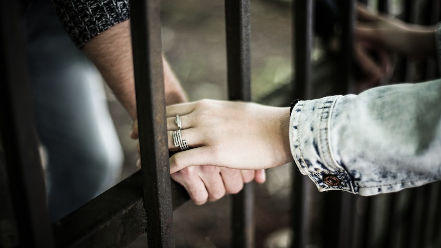 One person's hand resting upon another hand through a jail cell door