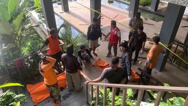 People standing around two orange body bags. 