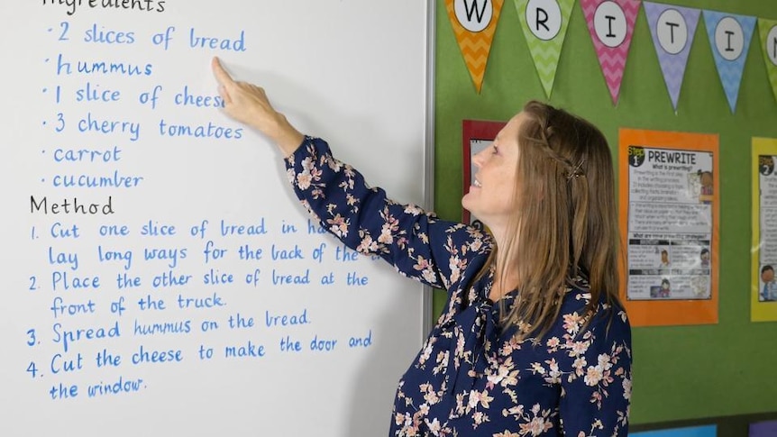 Female school teacher points to words on whiteboard