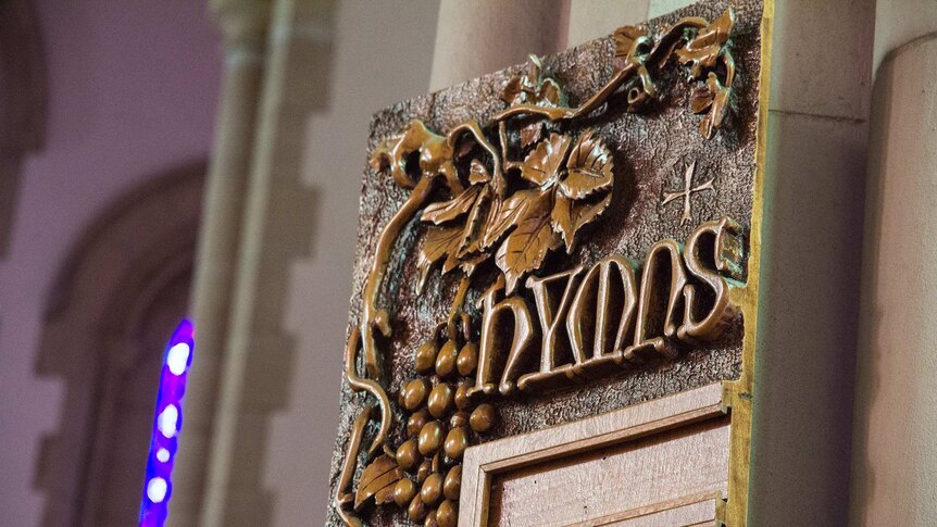 A wooden board inside a church reads 'hymns'