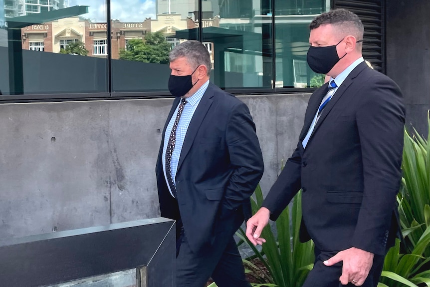 Two men in suits and black face masks outside the Brisbane courts complex