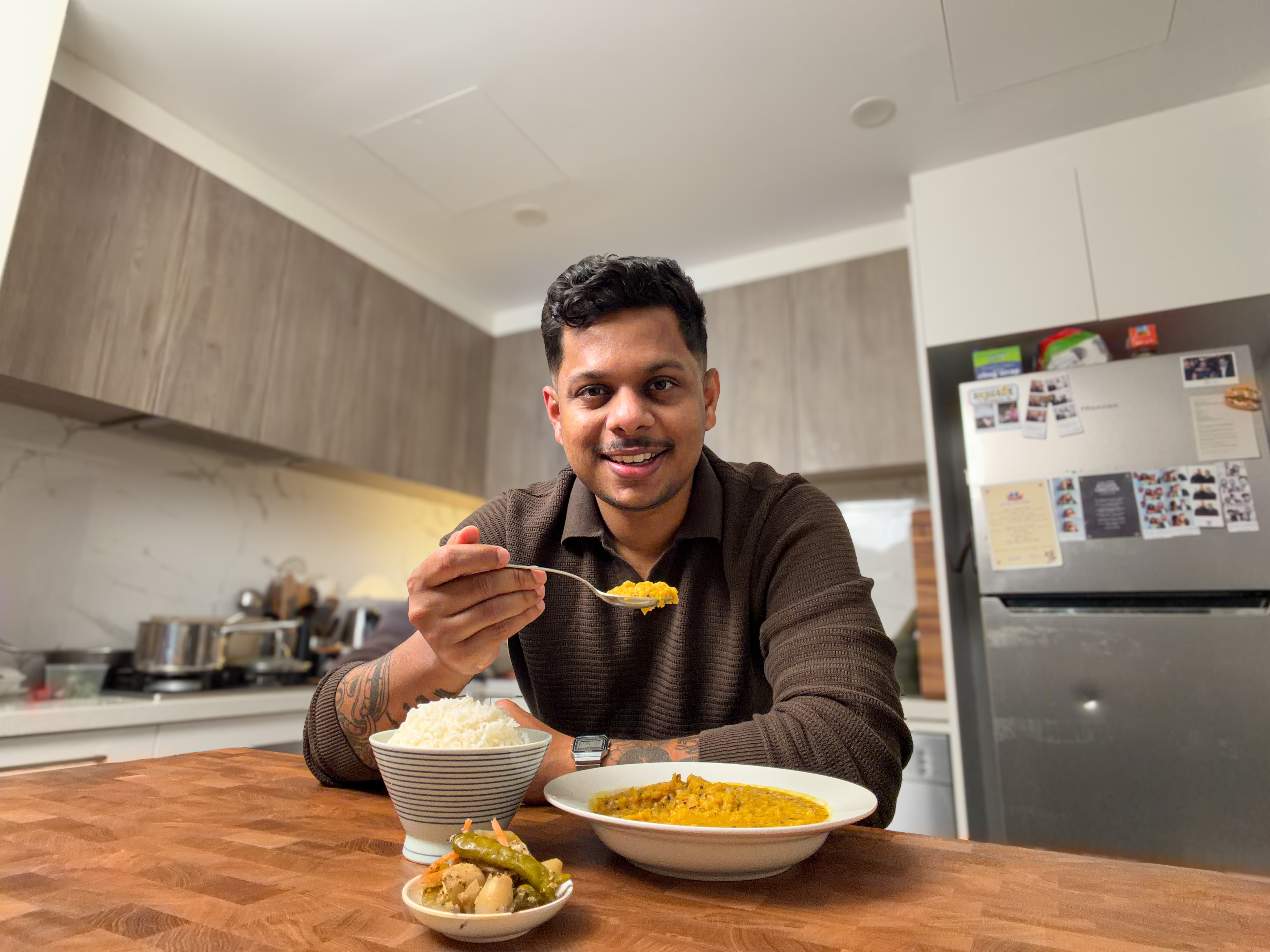 Nip Liyanapathirana sits behind a bowl of his dal, holding a spoonful and smiling.